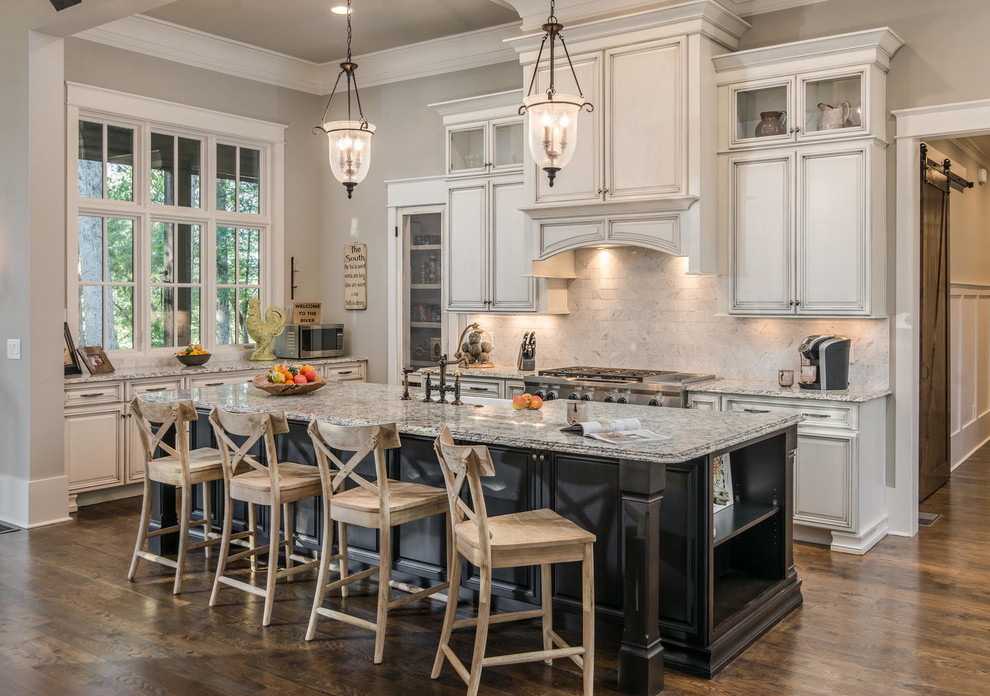 This is an example of a traditional galley kitchen in Other with a farmhouse sink, raised-panel cabinets, white cabinets, white splashback, stainless steel appliances, dark hardwood floors, with island and brown floor.
