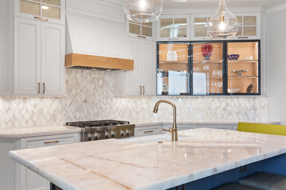 Inspiration for a large transitional single-wall light wood floor and brown floor eat-in kitchen remodel in Houston with a farmhouse sink, recessed-panel cabinets, white cabinets, quartzite countertops, white backsplash, mosaic tile backsplash, stainless steel appliances, an island and white countertops
