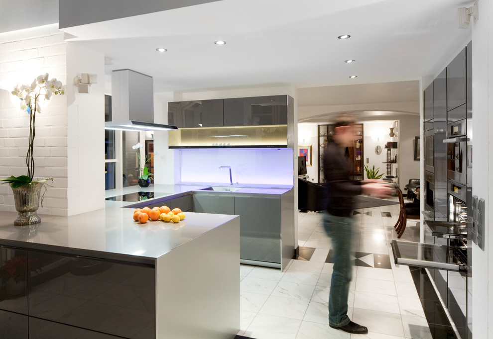 Large contemporary u-shaped open plan kitchen in Other with an undermount sink, flat-panel cabinets, grey cabinets, soapstone benchtops, white splashback, glass sheet splashback, stainless steel appliances, marble floors, a peninsula and grey benchtop.