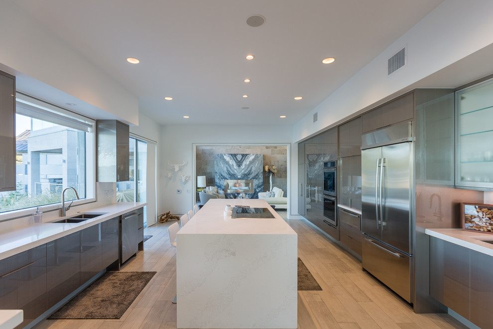 Large contemporary galley eat-in kitchen in Austin with an undermount sink, flat-panel cabinets, grey cabinets, white splashback, stainless steel appliances, light hardwood floors, with island and beige floor.