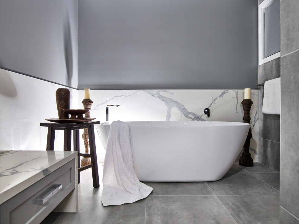 На фото: большая главная, серо-белая ванная комната в стиле модернизм с фасадами с утопленной филенкой, серыми фасадами, отдельно стоящей ванной, угловым душем, унитазом-моноблоком, плиткой из известняка, серыми стенами, полом из керамической плитки, настольной раковиной, столешницей из известняка, серым полом, душем с распашными дверями, белой столешницей, тумбой под одну раковину, встроенной тумбой и сводчатым потолком
