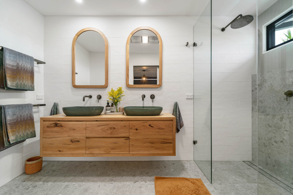 This is an example of a contemporary bathroom in Sydney with flat-panel cabinets, medium wood cabinets, a curbless shower, gray tile, white tile, white walls, a vessel sink, wood benchtops, grey floor, an open shower, brown benchtops, a double vanity and a floating vanity.