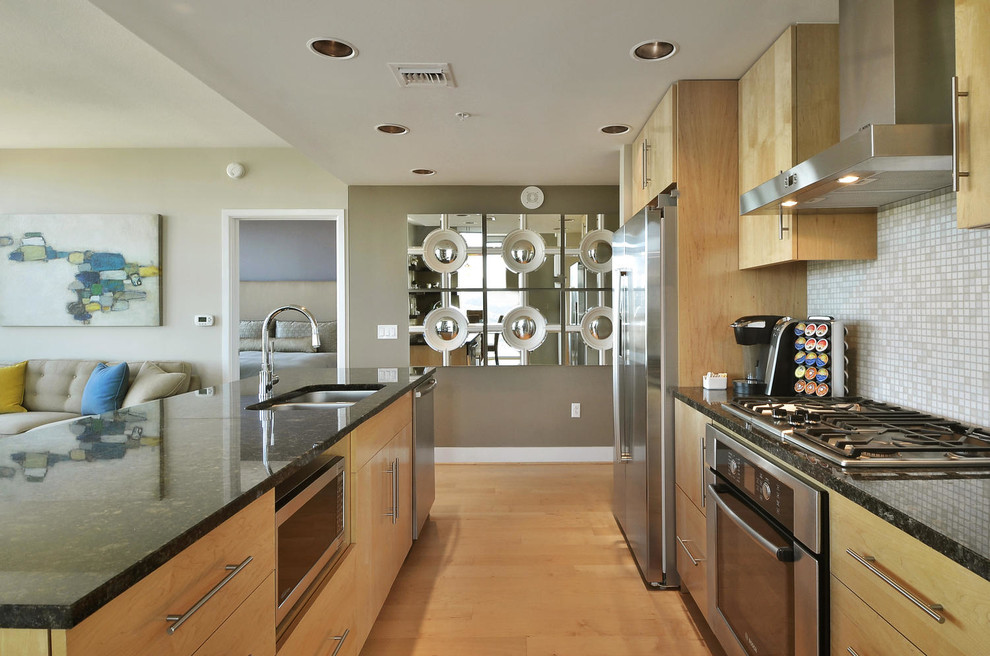 Small transitional galley light wood floor open concept kitchen photo in Austin with a double-bowl sink, flat-panel cabinets, light wood cabinets, granite countertops, beige backsplash, mosaic tile backsplash, stainless steel appliances and an island