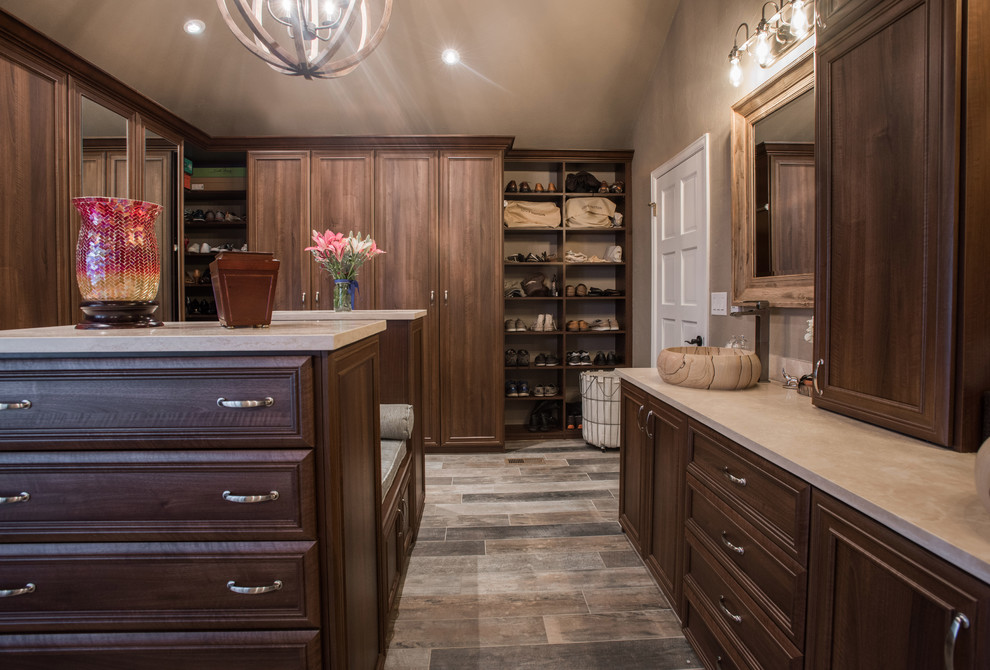 This is an example of a large traditional gender-neutral walk-in wardrobe in Denver with raised-panel cabinets, medium wood cabinets, plywood floors and brown floor.