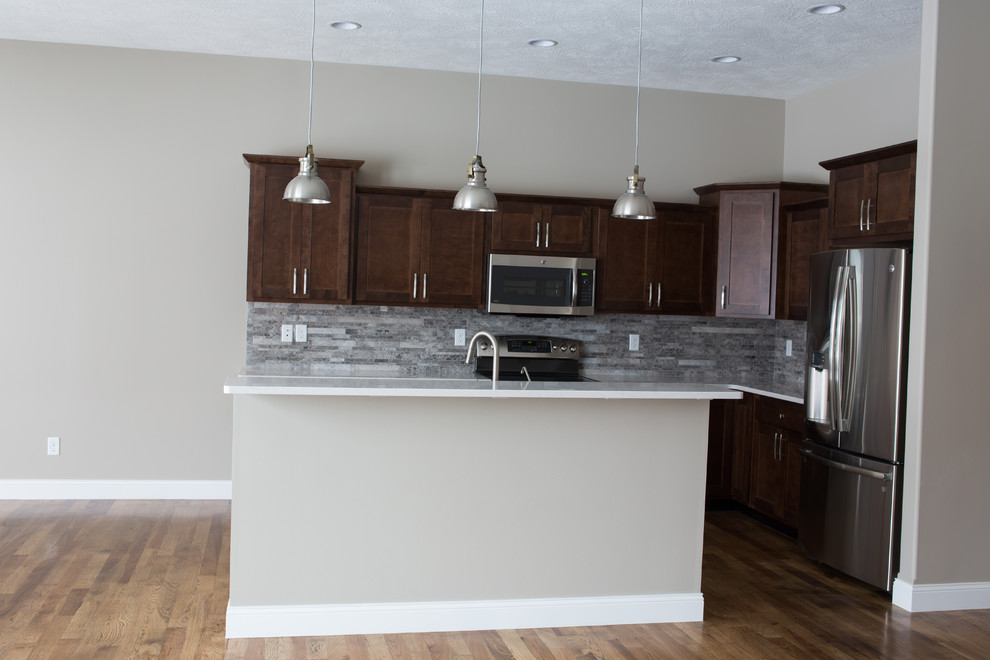 Inspiration for a mid-sized transitional l-shaped dark wood floor enclosed kitchen remodel with a double-bowl sink, shaker cabinets, dark wood cabinets, quartz countertops, gray backsplash, stone tile backsplash, stainless steel appliances and an island