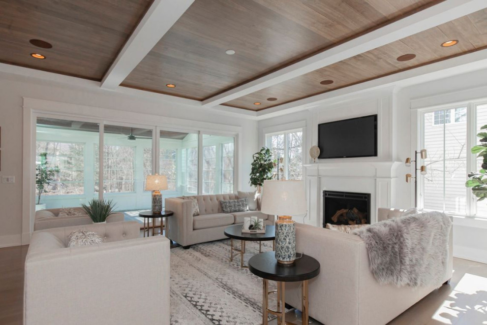 Large country open concept family room in Chicago with white walls, light hardwood floors, a standard fireplace, a wood fireplace surround, a wall-mounted tv, brown floor and exposed beam.