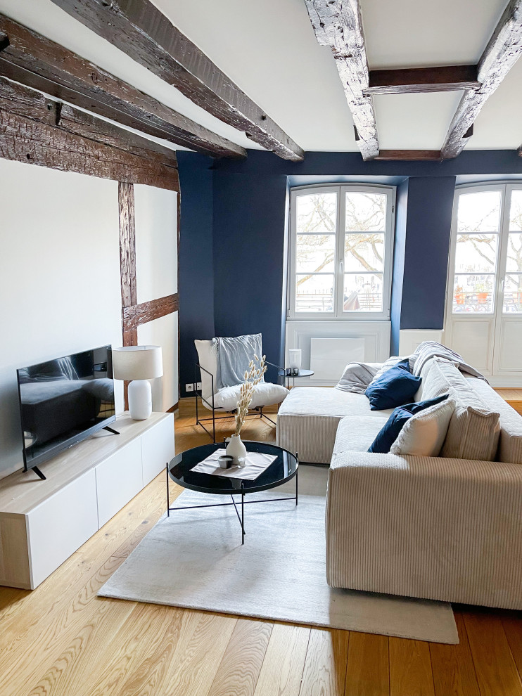 На фото: открытая гостиная комната среднего размера:: освещение в стиле неоклассика (современная классика) с синими стенами, светлым паркетным полом, отдельно стоящим телевизором, желтым полом и балками на потолке без камина