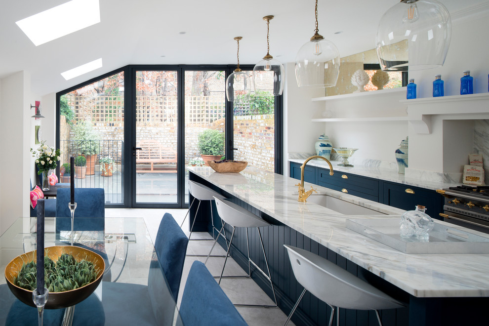 This is an example of a transitional eat-in kitchen in London with an undermount sink, blue cabinets, with island and multi-coloured benchtop.
