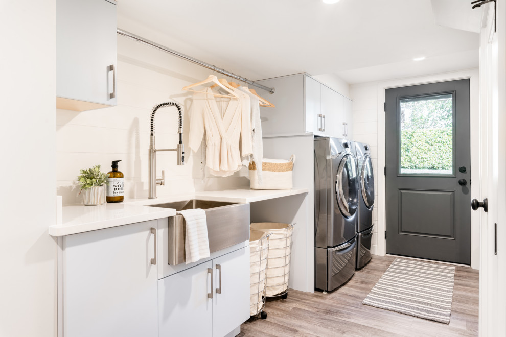 Mid-sized contemporary single-wall dedicated laundry room in Other with a farmhouse sink, flat-panel cabinets, white cabinets, white walls, medium hardwood floors, a side-by-side washer and dryer, brown floor and white benchtop.