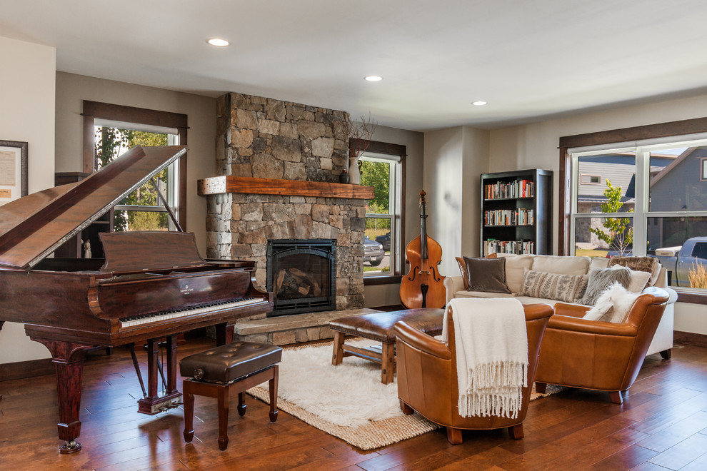 Photo of a country living room in Other with a music area, grey walls, medium hardwood floors, a standard fireplace, a stone fireplace surround and brown floor.