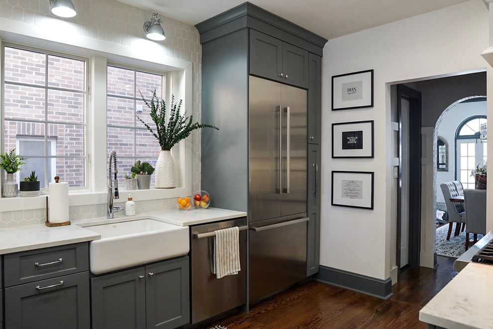 This is an example of a mid-sized transitional kitchen in Chicago with a farmhouse sink, quartz benchtops, white splashback, cement tile splashback, stainless steel appliances, dark hardwood floors, brown floor, white benchtop, shaker cabinets and grey cabinets.