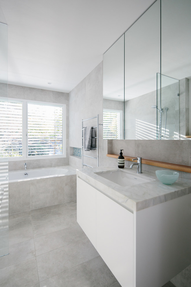 Photo of a mid-sized contemporary 3/4 bathroom in Other with recessed-panel cabinets, white cabinets, a drop-in tub, an open shower, a wall-mount toilet, gray tile, stone tile, ceramic floors, an undermount sink, engineered quartz benchtops and an open shower.