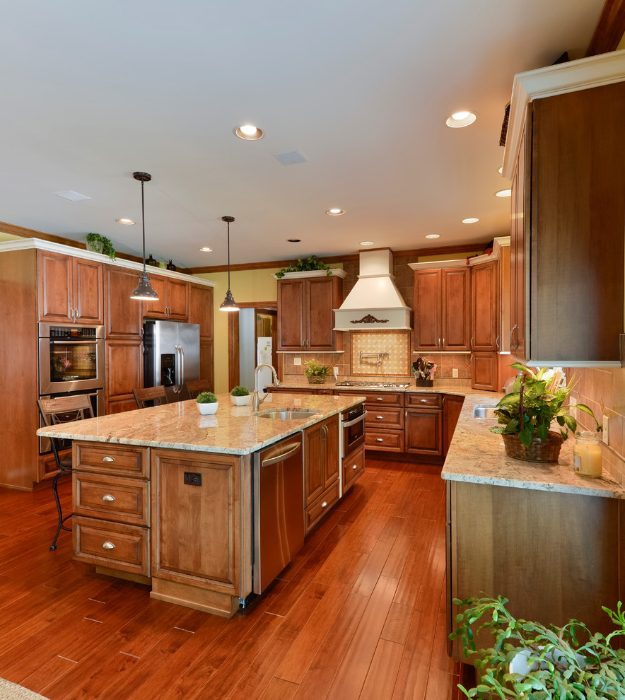 Large transitional u-shaped medium tone wood floor eat-in kitchen photo with beaded inset cabinets, medium tone wood cabinets, granite countertops, beige backsplash, mosaic tile backsplash, stainless steel appliances and an island