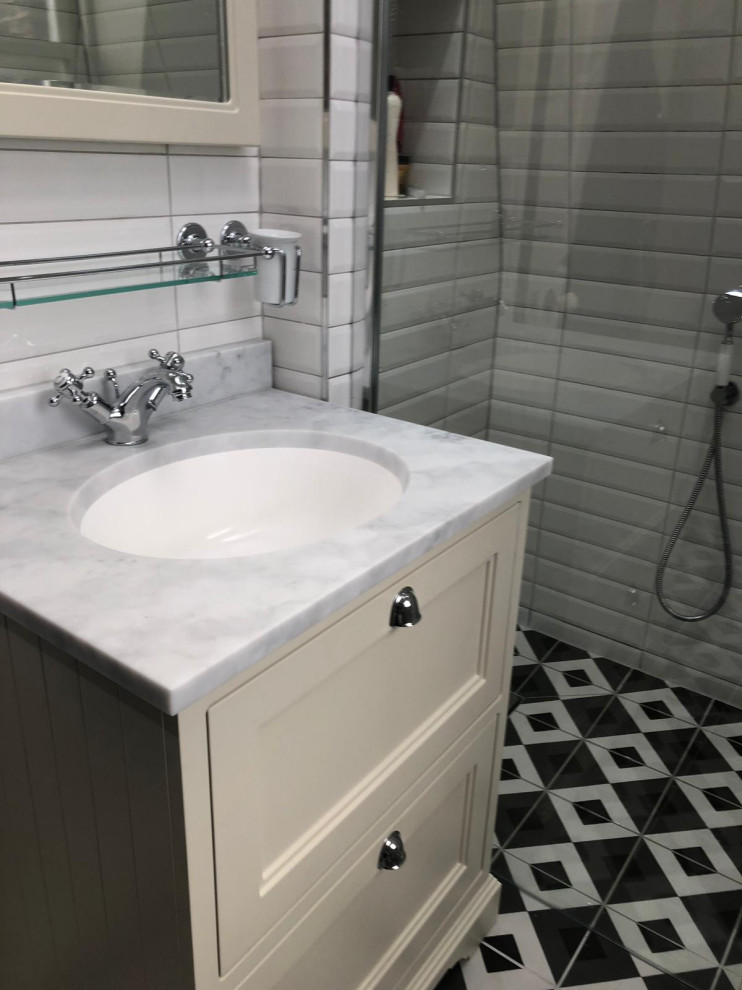 Mid-sized traditional master bathroom in London with shaker cabinets, beige cabinets, an open shower, a two-piece toilet, white tile, ceramic tile, grey walls, mosaic tile floors, an undermount sink, solid surface benchtops, multi-coloured floor, grey benchtops, a single vanity and a freestanding vanity.
