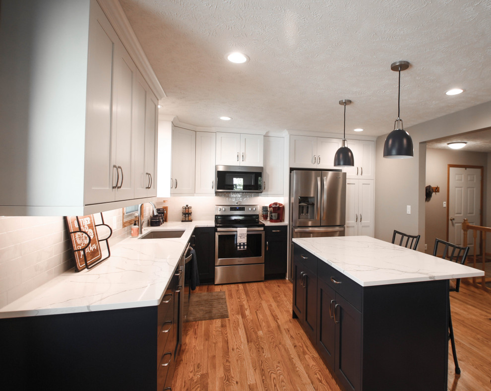 Example of a mid-sized transitional u-shaped medium tone wood floor kitchen pantry design with an undermount sink, shaker cabinets, blue cabinets, quartz countertops, gray backsplash, ceramic backsplash, stainless steel appliances, an island and white countertops