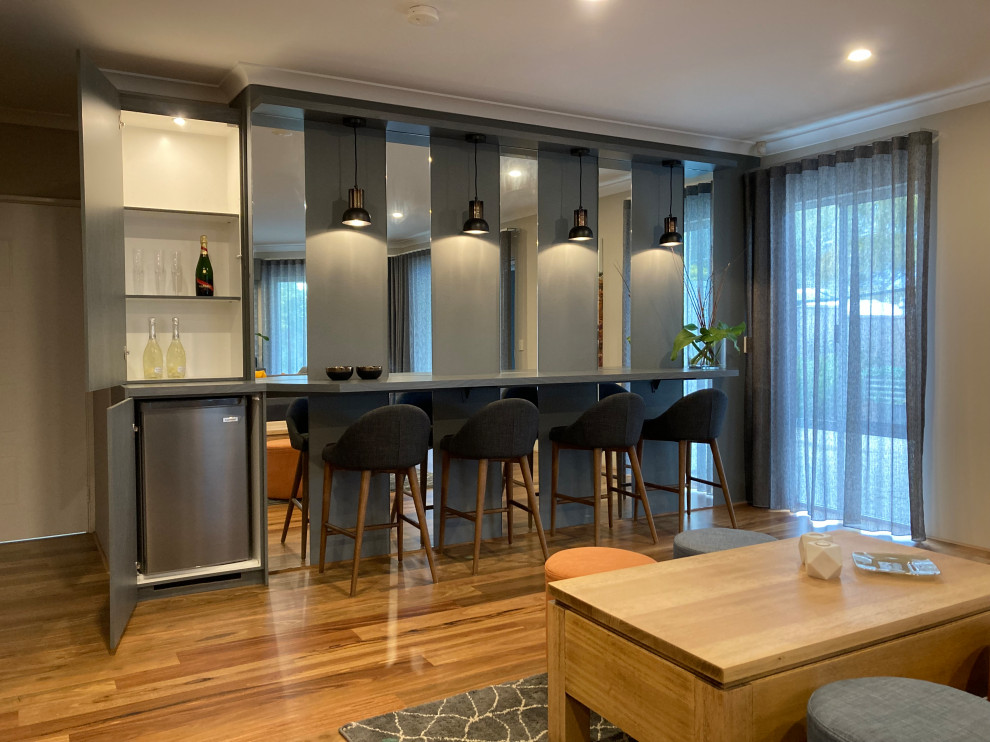 This is an example of an expansive contemporary galley home bar in Perth with flat-panel cabinets, grey cabinets, laminate benchtops, mirror splashback, medium hardwood floors, brown floor and grey benchtop.