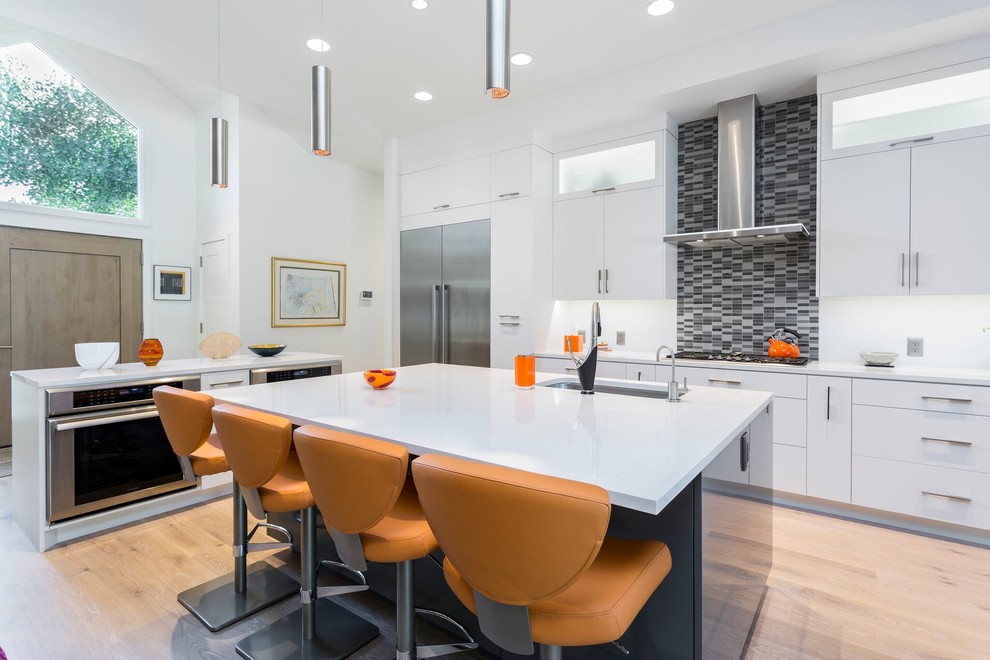 Photo of a large contemporary l-shaped kitchen in Salt Lake City with an undermount sink, flat-panel cabinets, white cabinets, grey splashback, mosaic tile splashback, stainless steel appliances, light hardwood floors, multiple islands, beige floor, white benchtop and solid surface benchtops.