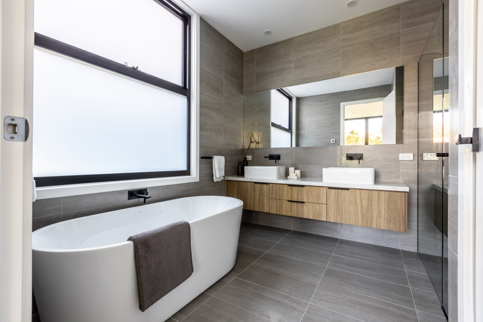 Mid-sized contemporary kids bathroom in Melbourne with light wood cabinets, a freestanding tub, a double shower, a one-piece toilet, gray tile, porcelain tile, grey walls, porcelain floors, a console sink, marble benchtops, grey floor, a hinged shower door, white benchtops, a niche, a double vanity and a floating vanity.