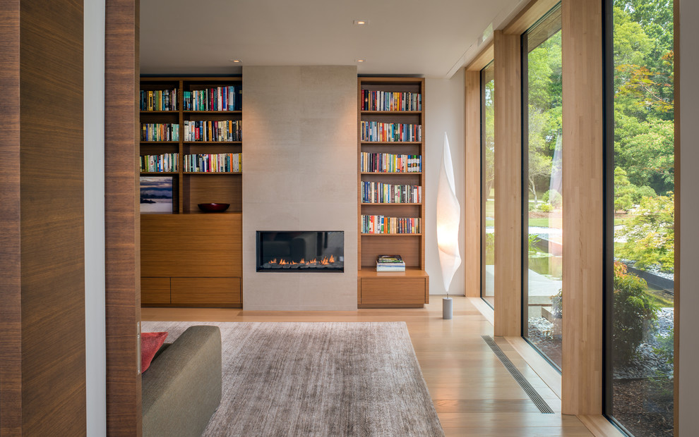 Photo of a contemporary open concept family room in Other with a library, white walls, light hardwood floors, a standard fireplace, a tile fireplace surround and a concealed tv.