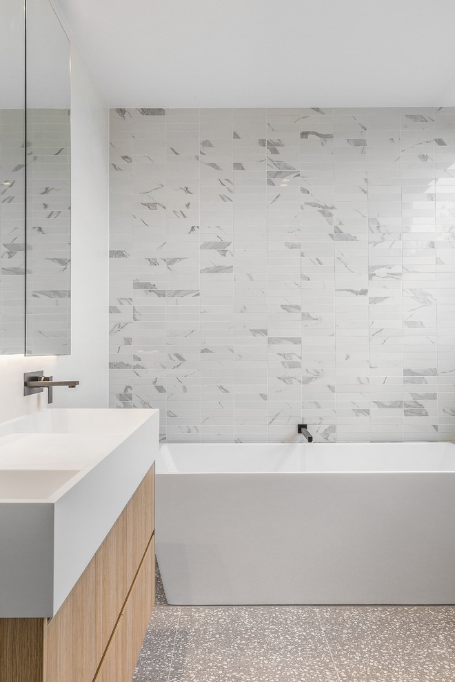 This is an example of a mid-sized modern kids bathroom in Melbourne with flat-panel cabinets, light wood cabinets, a freestanding tub, a corner shower, white tile, mosaic tile, white walls, terrazzo floors, an integrated sink, marble benchtops, grey floor, a hinged shower door and white benchtops.