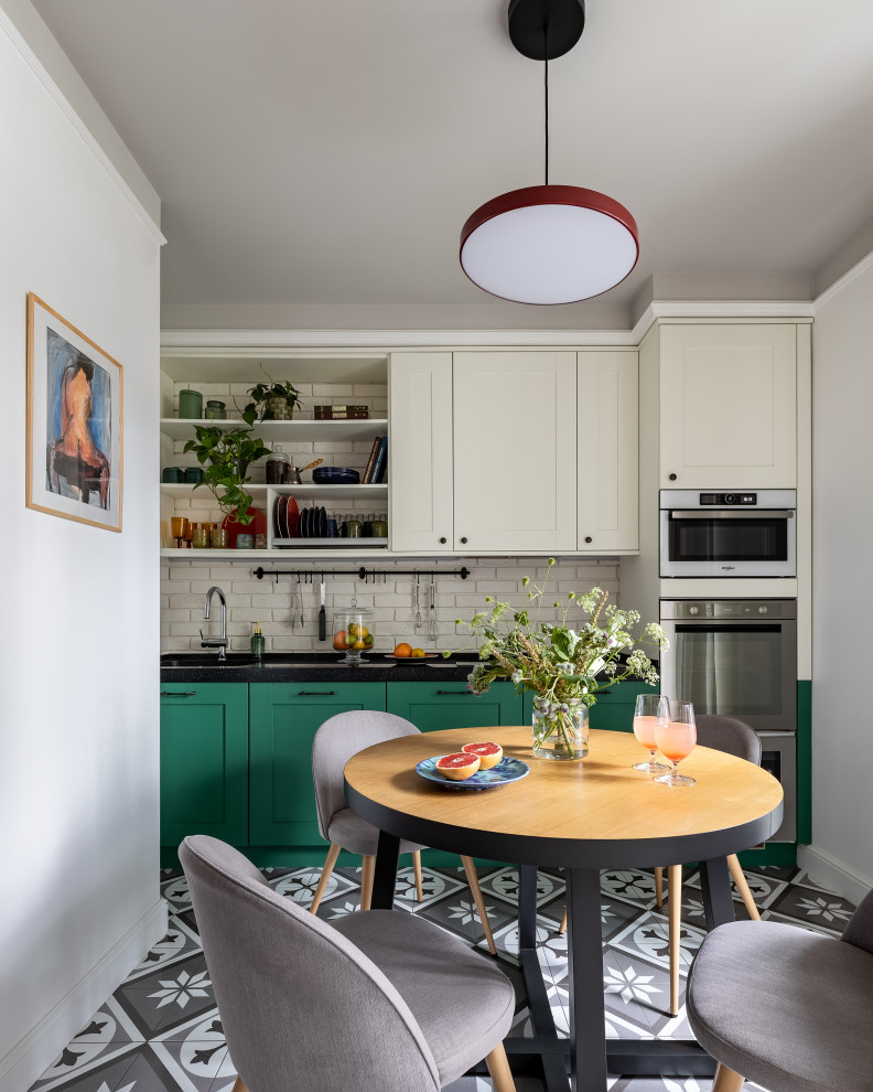 Transitional kitchen in Moscow with recessed-panel cabinets, green cabinets, white splashback, stainless steel appliances, multi-coloured floor and black benchtop.