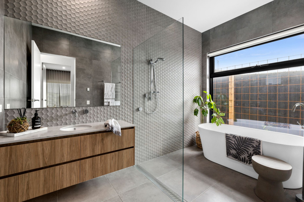 Inspiration for a large contemporary wet room bathroom in Geelong with flat-panel cabinets, light wood cabinets, a freestanding bath, grey tiles, porcelain tiles, a submerged sink, engineered stone worktops, an open shower, grey worktops, a single sink and a built in vanity unit.