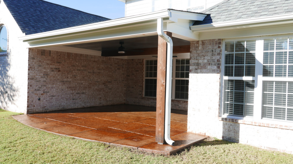 This is an example of a mid-sized traditional backyard verandah in Other with with columns, stamped concrete and a roof extension.