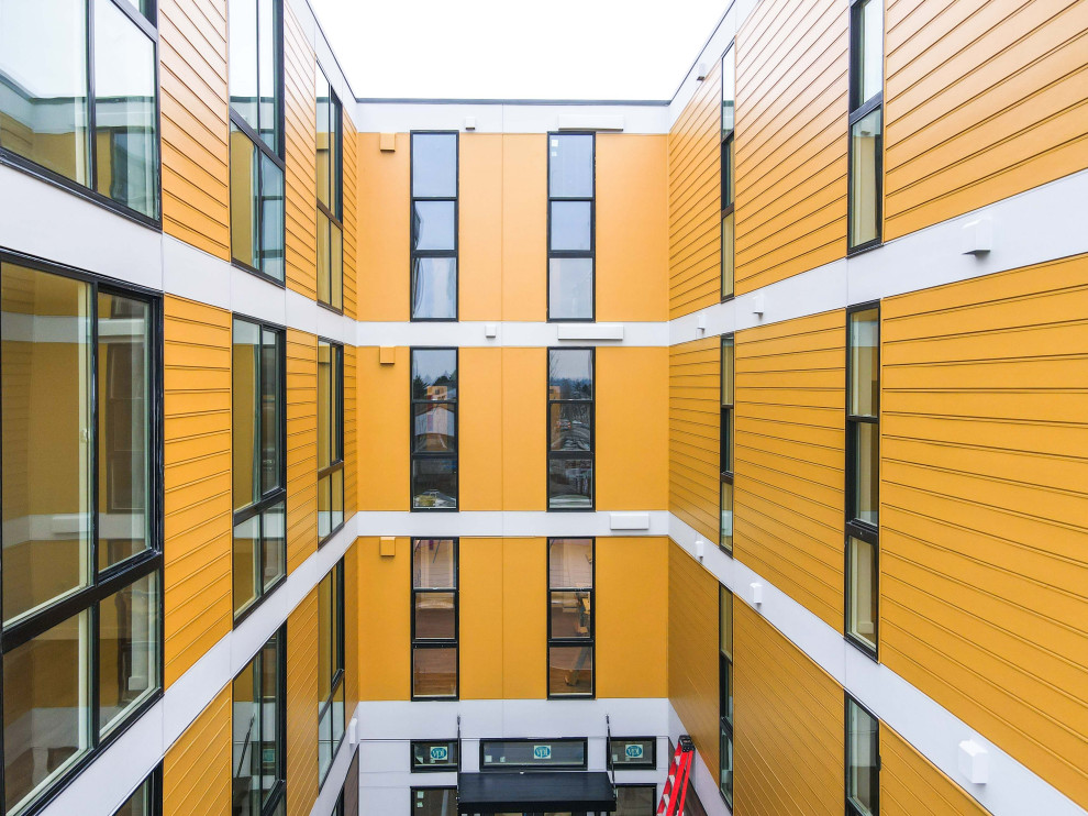 Immagine della facciata di un appartamento ampio arancione moderno a quattro piani con rivestimento con lastre in cemento, tetto piano, copertura mista, tetto bianco e pannelli e listelle di legno