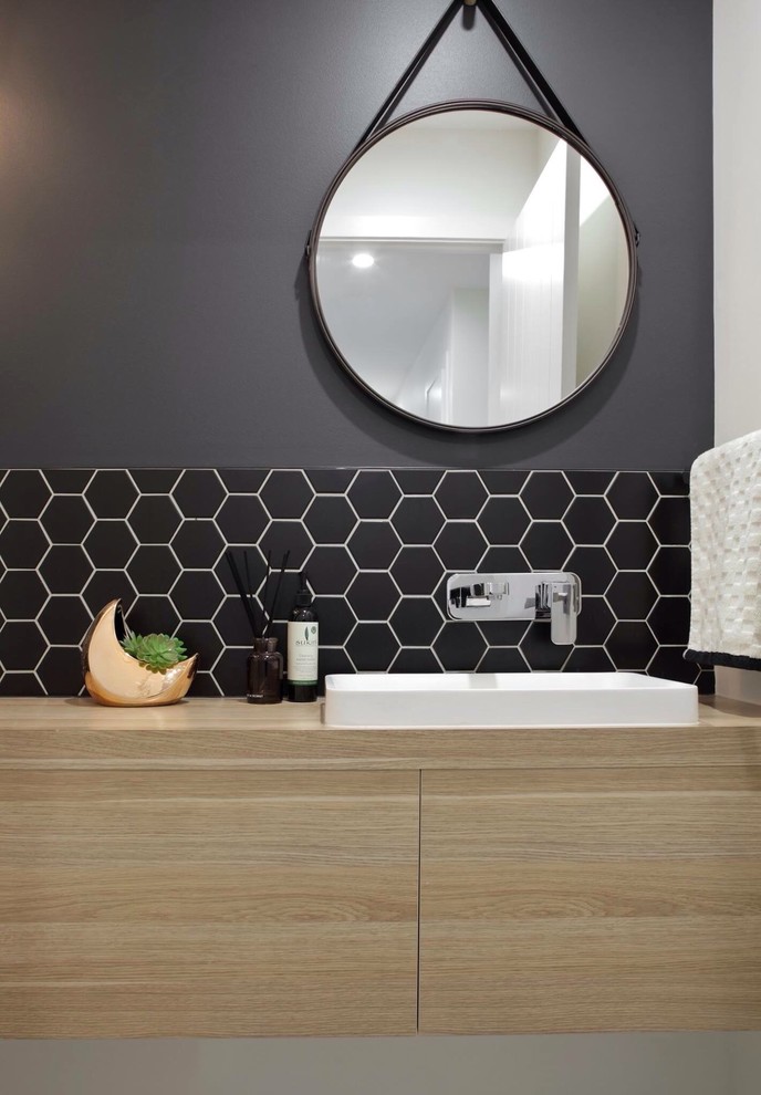 Inspiration for a modern powder room in Sunshine Coast with light wood cabinets, a wall-mount toilet, black tile, mosaic tile, black walls, laminate benchtops and a drop-in sink.