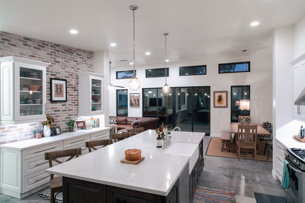 This is an example of a large transitional galley open plan kitchen in Phoenix with a farmhouse sink, white cabinets, quartzite benchtops, brick splashback, stainless steel appliances, concrete floors, with island, grey floor, white benchtop, raised-panel cabinets and multi-coloured splashback.