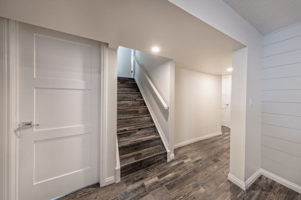 Photo of a mid-sized modern fully buried basement in Edmonton with a home bar, white walls, vinyl floors, a standard fireplace, a tile fireplace surround, brown floor and planked wall panelling.