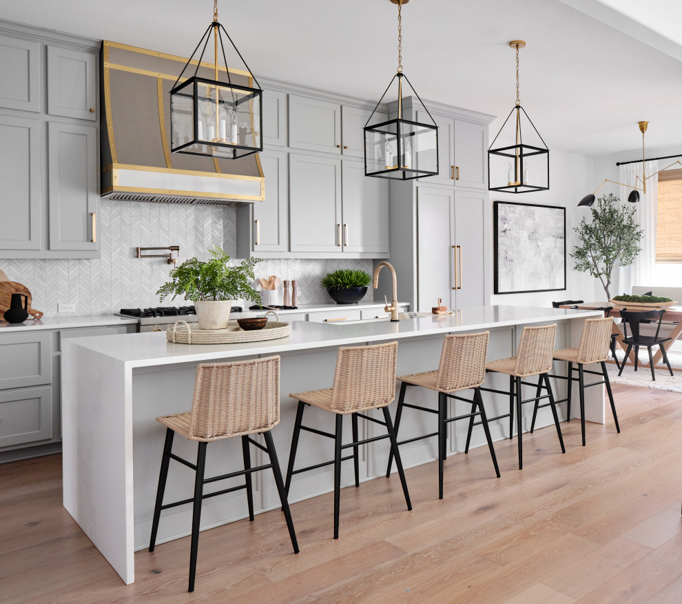 Design ideas for a mid-sized transitional l-shaped open plan kitchen in Austin with a farmhouse sink, shaker cabinets, grey cabinets, quartz benchtops, grey splashback, marble splashback, panelled appliances, light hardwood floors, with island, grey floor and white benchtop.