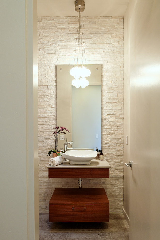 Small contemporary powder room in Albuquerque with flat-panel cabinets, medium wood cabinets, beige tile, stone tile, beige walls, porcelain floors, a vessel sink, brown floor and beige benchtops.
