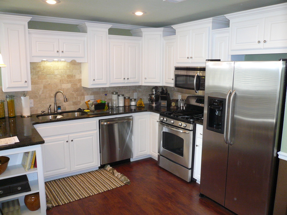 U-shaped eat-in kitchen photo with an undermount sink, raised-panel cabinets, white cabinets, granite countertops, beige backsplash, stone tile backsplash, stainless steel appliances, green walls, engineered wood floors and an island