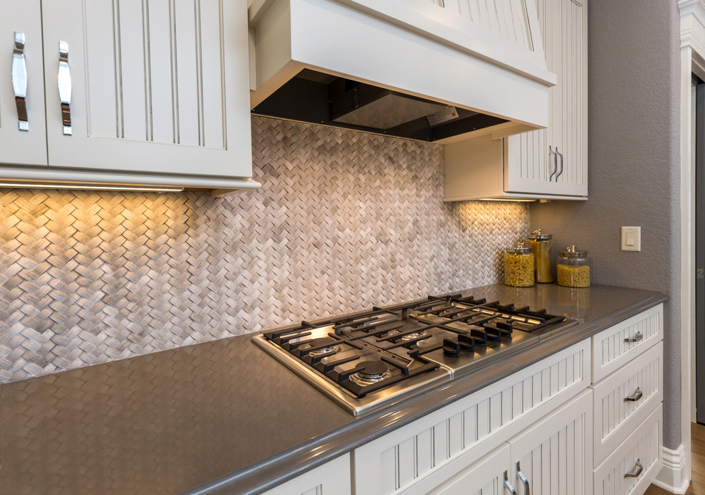 Example of a transitional l-shaped kitchen pantry design with an undermount sink, beaded inset cabinets, white cabinets, quartz countertops, beige backsplash, stone tile backsplash, stainless steel appliances and an island
