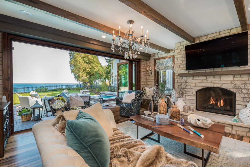Inspiration for a mid-sized transitional open concept family room in Milwaukee with grey walls, medium hardwood floors, a standard fireplace, a stone fireplace surround, a wall-mounted tv, multi-coloured floor, exposed beam and brick walls.
