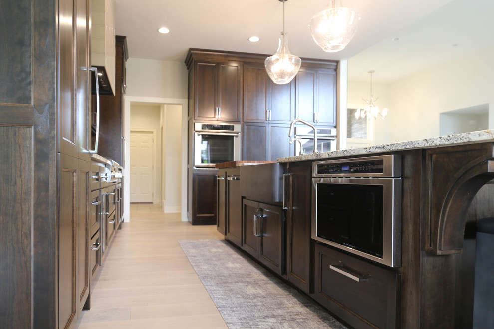 Inspiration for a large transitional l-shaped light wood floor and beige floor eat-in kitchen remodel with a farmhouse sink, recessed-panel cabinets, dark wood cabinets, granite countertops, gray backsplash, porcelain backsplash, stainless steel appliances, an island and multicolored countertops
