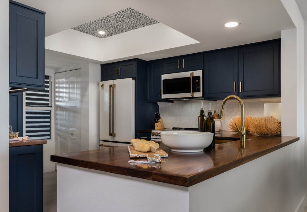 Design ideas for a large beach style l-shaped separate kitchen in Tampa with a drop-in sink, flat-panel cabinets, blue cabinets, wood benchtops, white splashback, ceramic splashback, stainless steel appliances, limestone floors, beige floor and brown benchtop.