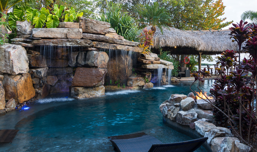 Inspiration for an expansive tropical backyard custom-shaped natural pool in Tampa with a water feature and natural stone pavers.