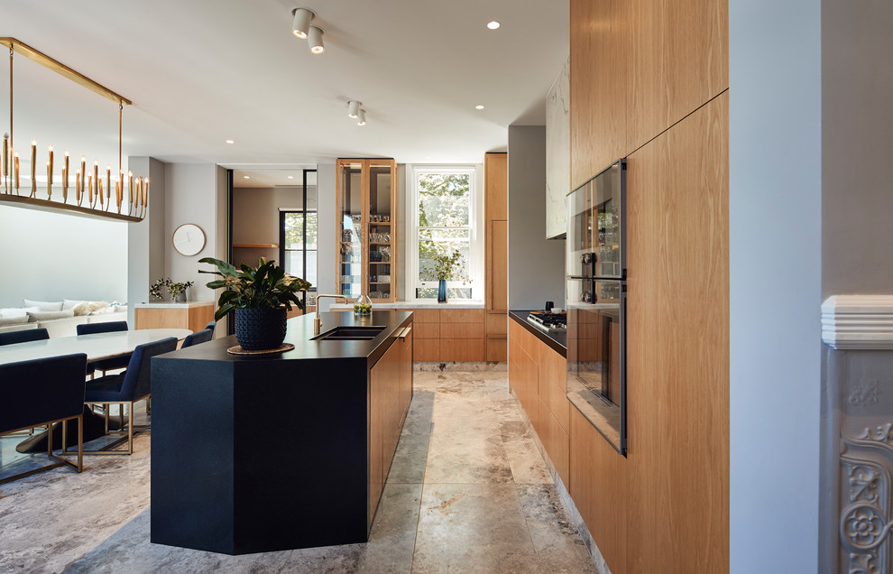 This is an example of a mid-sized contemporary l-shaped open plan kitchen in Melbourne with an undermount sink, flat-panel cabinets, medium wood cabinets, granite benchtops, white splashback, marble splashback, panelled appliances, limestone floors, with island, grey floor and black benchtop.
