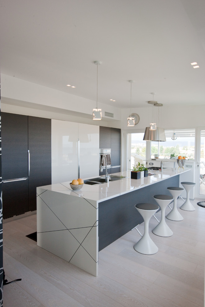 Photo of a large contemporary single-wall open plan kitchen in Other with a drop-in sink, flat-panel cabinets, white cabinets, solid surface benchtops, light hardwood floors and with island.