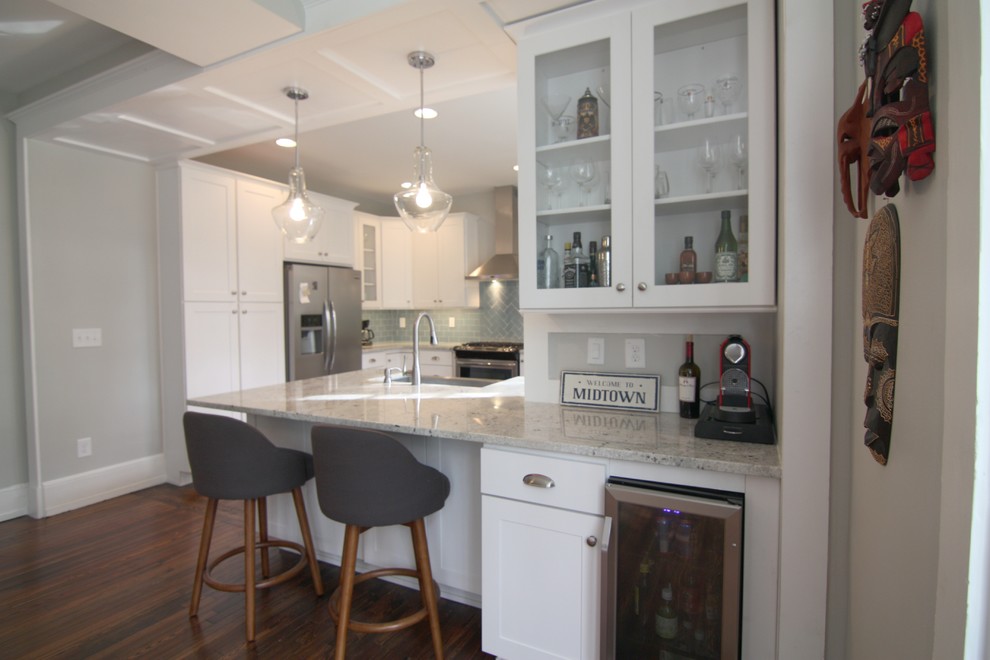 This is an example of a mid-sized arts and crafts l-shaped eat-in kitchen in Atlanta with a farmhouse sink, shaker cabinets, white cabinets, granite benchtops, blue splashback, glass tile splashback, stainless steel appliances, medium hardwood floors and a peninsula.