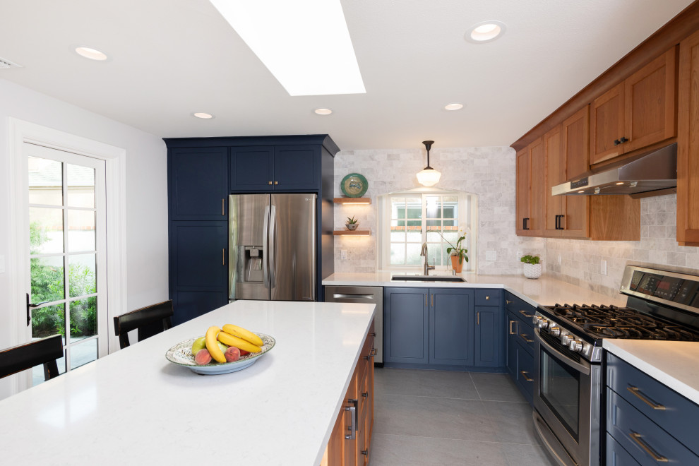 Mid-sized transitional l-shaped ceramic tile and gray floor enclosed kitchen photo in Orange County with an undermount sink, shaker cabinets, blue cabinets, quartz countertops, gray backsplash, marble backsplash, stainless steel appliances, an island and white countertops