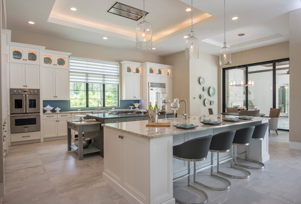 This is an example of a transitional l-shaped eat-in kitchen in Orlando with white cabinets, marble benchtops, blue splashback, stainless steel appliances, porcelain floors, multiple islands, grey floor, beige benchtop, a farmhouse sink, recessed-panel cabinets and glass tile splashback.