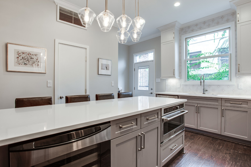 Large transitional l-shaped medium tone wood floor and brown floor eat-in kitchen photo in DC Metro with an undermount sink, shaker cabinets, white cabinets, solid surface countertops, white backsplash, ceramic backsplash, stainless steel appliances, an island and white countertops