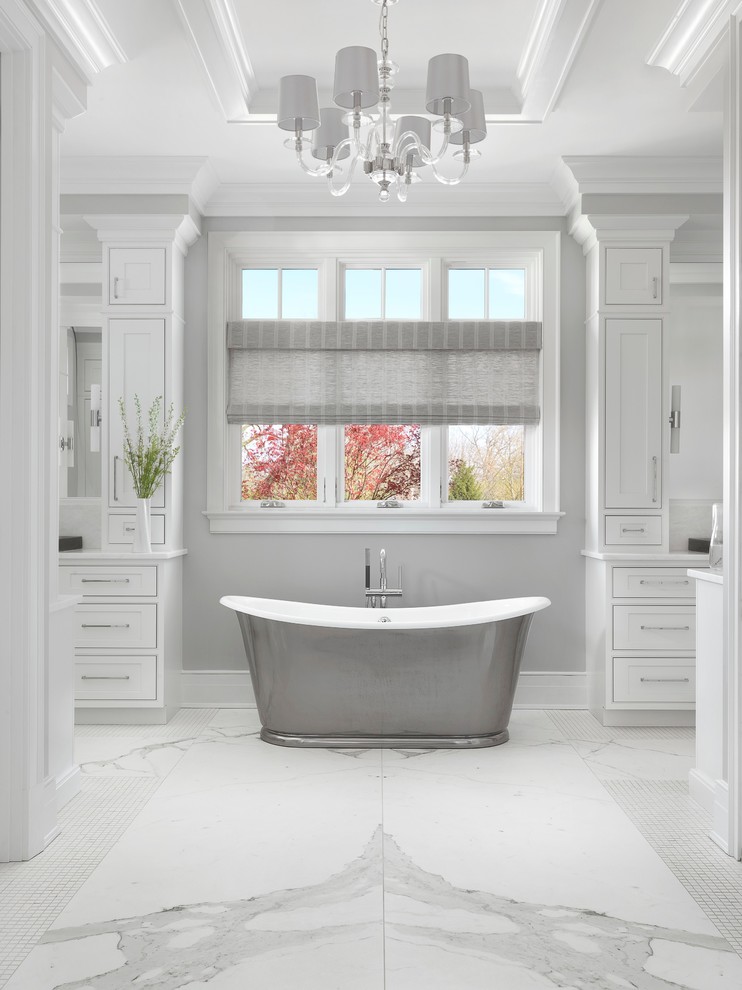 This is an example of a large traditional master bathroom in St Louis with a freestanding tub, white walls, marble floors, white floor, beaded inset cabinets and white cabinets.