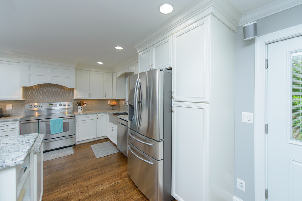Large transitional l-shaped dark wood floor and brown floor kitchen photo in Baltimore with a farmhouse sink, recessed-panel cabinets, white cabinets, quartz countertops, gray backsplash, subway tile backsplash, stainless steel appliances and an island