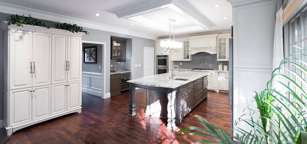This is an example of a large traditional u-shaped eat-in kitchen in Philadelphia with an undermount sink, raised-panel cabinets, white cabinets, quartzite benchtops, grey splashback, glass tile splashback, stainless steel appliances, medium hardwood floors, with island and brown floor.