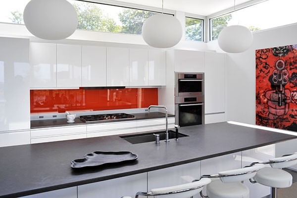 Photo of a mid-sized modern galley open plan kitchen in New York with an undermount sink, flat-panel cabinets, white cabinets, solid surface benchtops, glass sheet splashback, stainless steel appliances, porcelain floors, with island and red splashback.