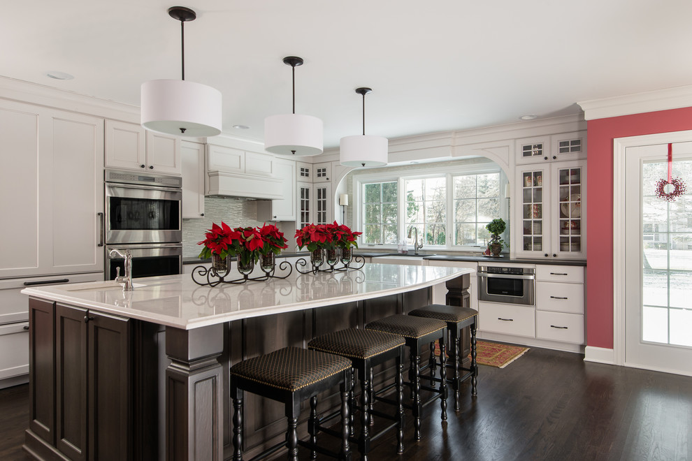 Photo of a large transitional l-shaped eat-in kitchen in Detroit with a farmhouse sink, white cabinets, quartz benchtops, white splashback, dark hardwood floors, with island, multi-coloured benchtop, recessed-panel cabinets, glass tile splashback, stainless steel appliances and black floor.